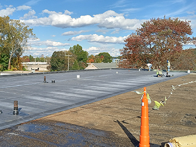 Flat commercial roof installation in progress, with roofing crew applying membrane, and safety markers around the rooftop