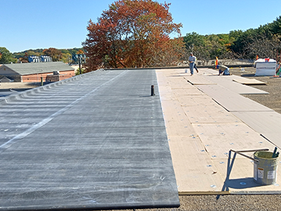 Roofing workers installing flat commercial roofing membrane on large building roof