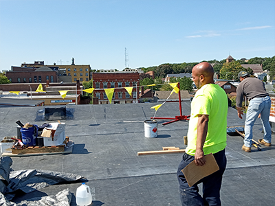 Roofing crew installing a flat commercial roof on a rooftop overlooking nearby buildings