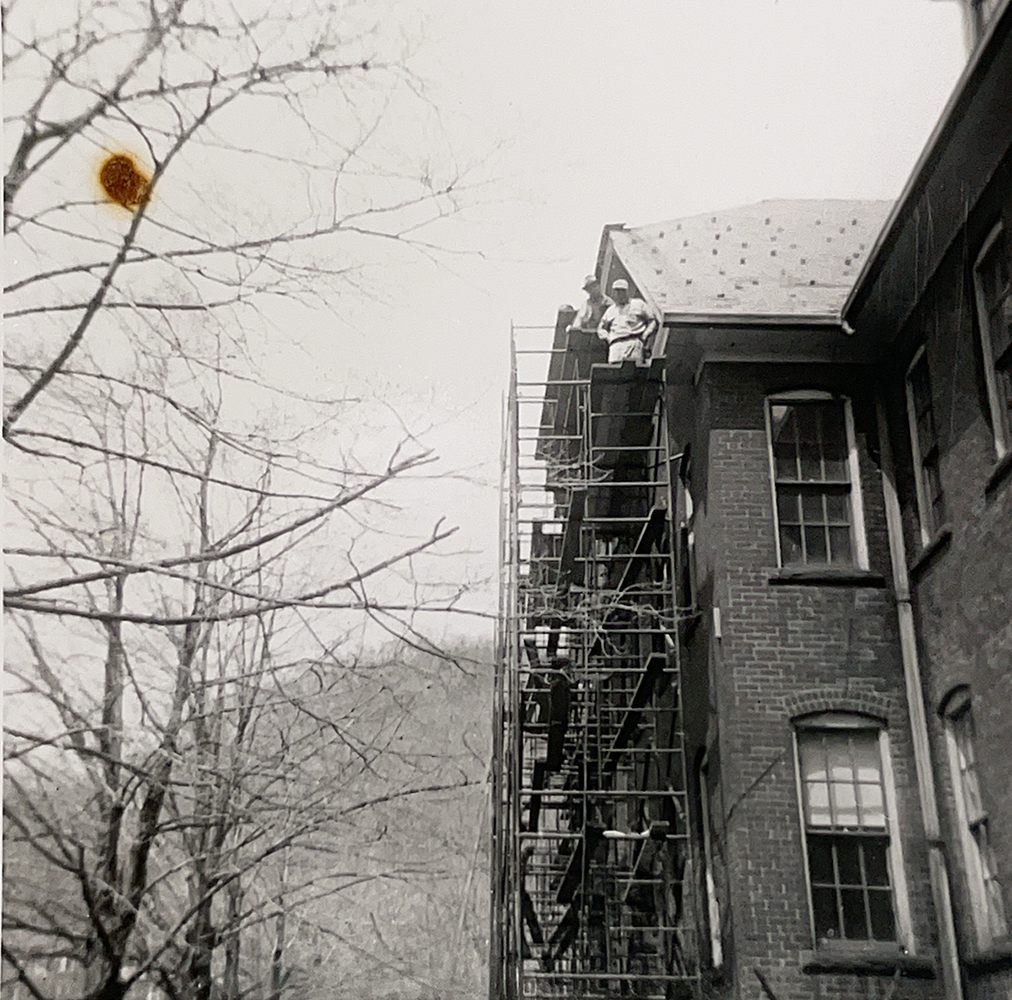 Black-and-white photo of workers on scaffolding working on the roof of a brick building