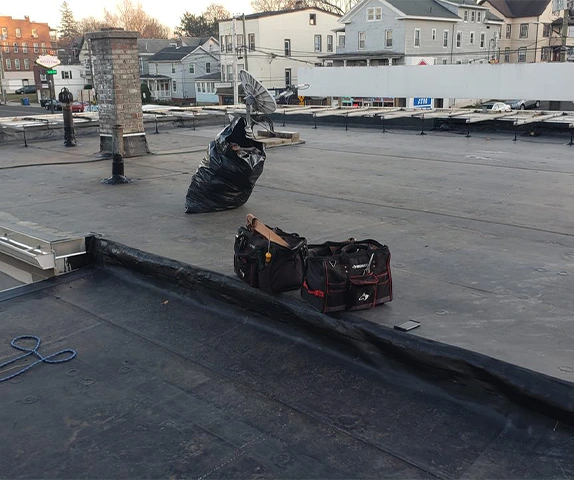 Tool bags on a flat rooftop with nearby vent pipe and residential buildings in the background
