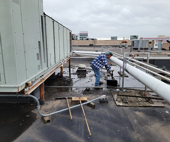 Worker cleaning rooftop near HVAC equipment and piping