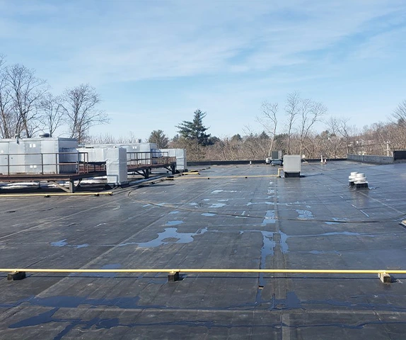 Large flat commercial roof undergoing repair with HVAC units and small puddles of water