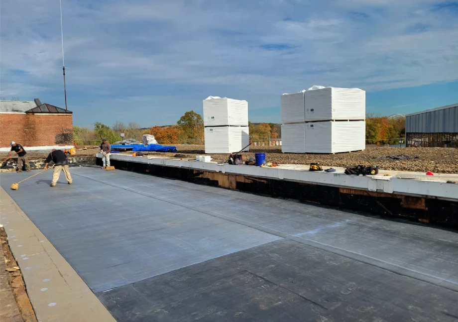 Roofing workers applying flat roof membrane on large commercial building rooftop