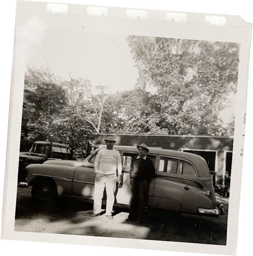Black-and-white photo of two men standing beside a vintage car in a driveway
