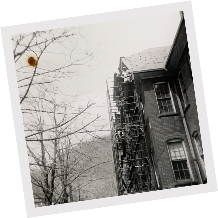 Black-and-white photo of workers on scaffolding working on the roof of a brick building