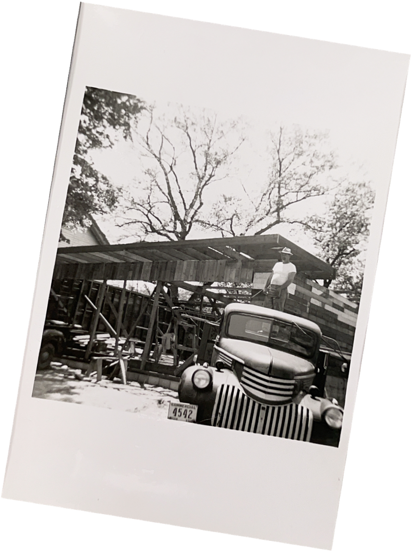 Black-and-white photo of a man standing on a vintage truck to frame a roof